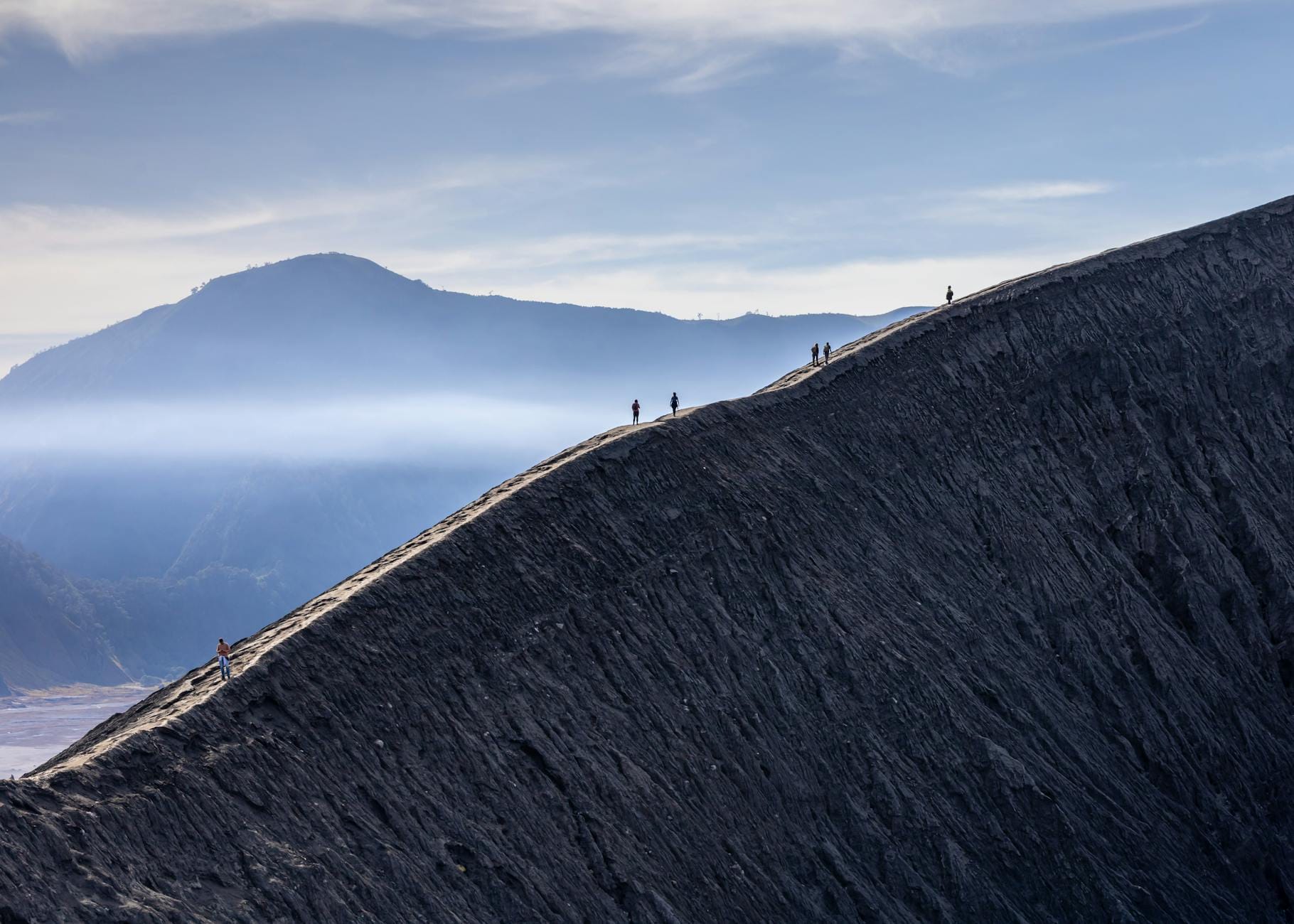Turyści idą granią wulkanu Bromo z widokiem na dymiący krater