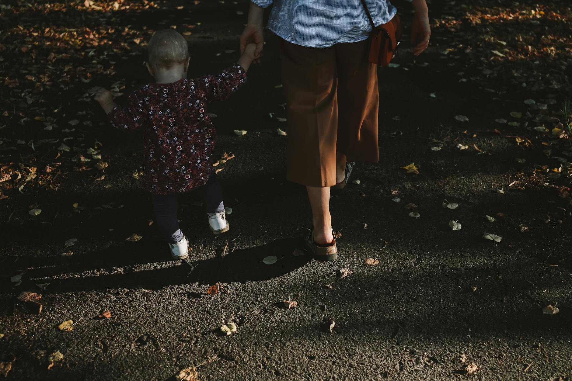 Mama z kilkuletnim dzieckiem spacerują jesienną alejką pełną liści