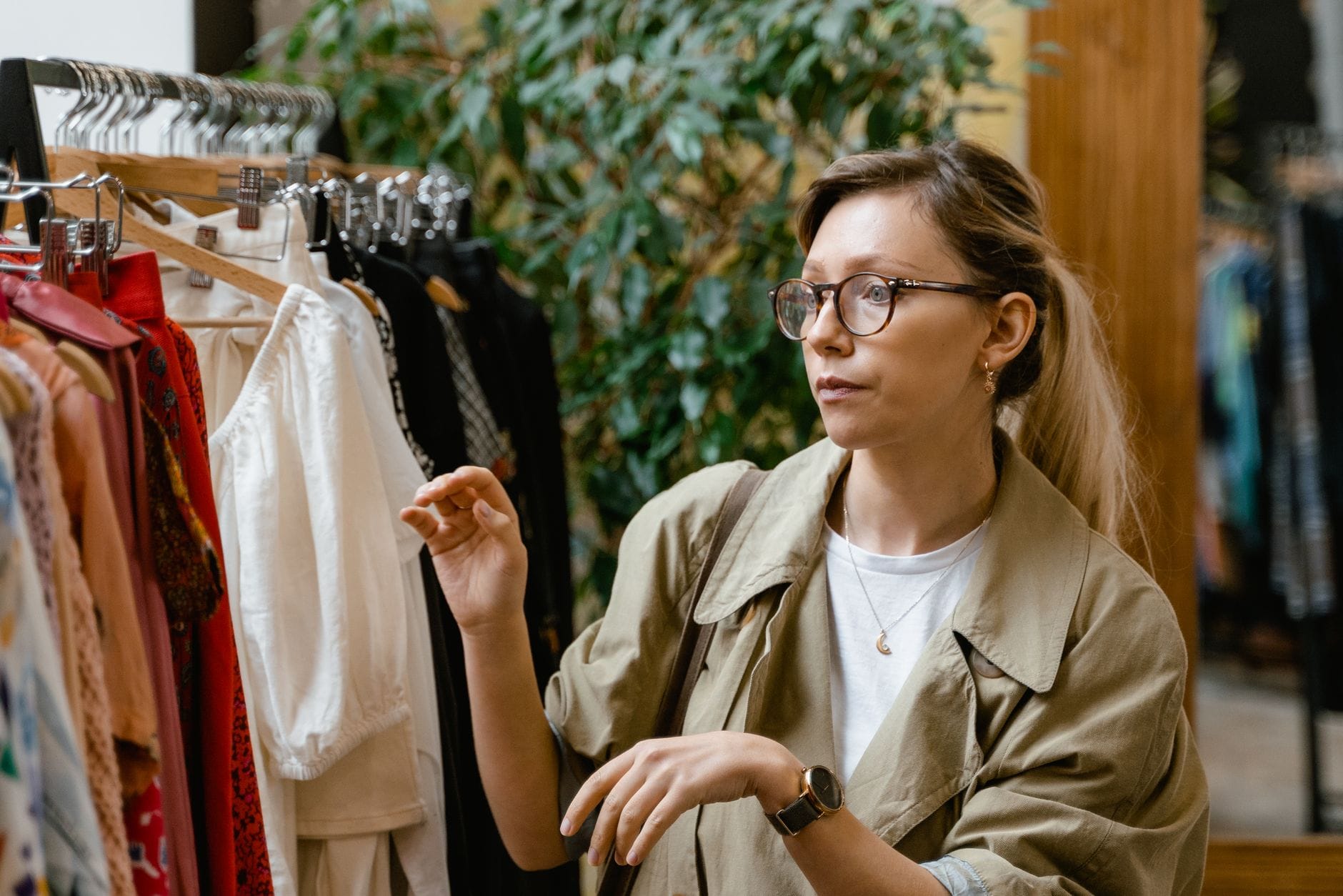 Kobieta w okularach ogląda ubrania na wieszaku w eleganckim butiku