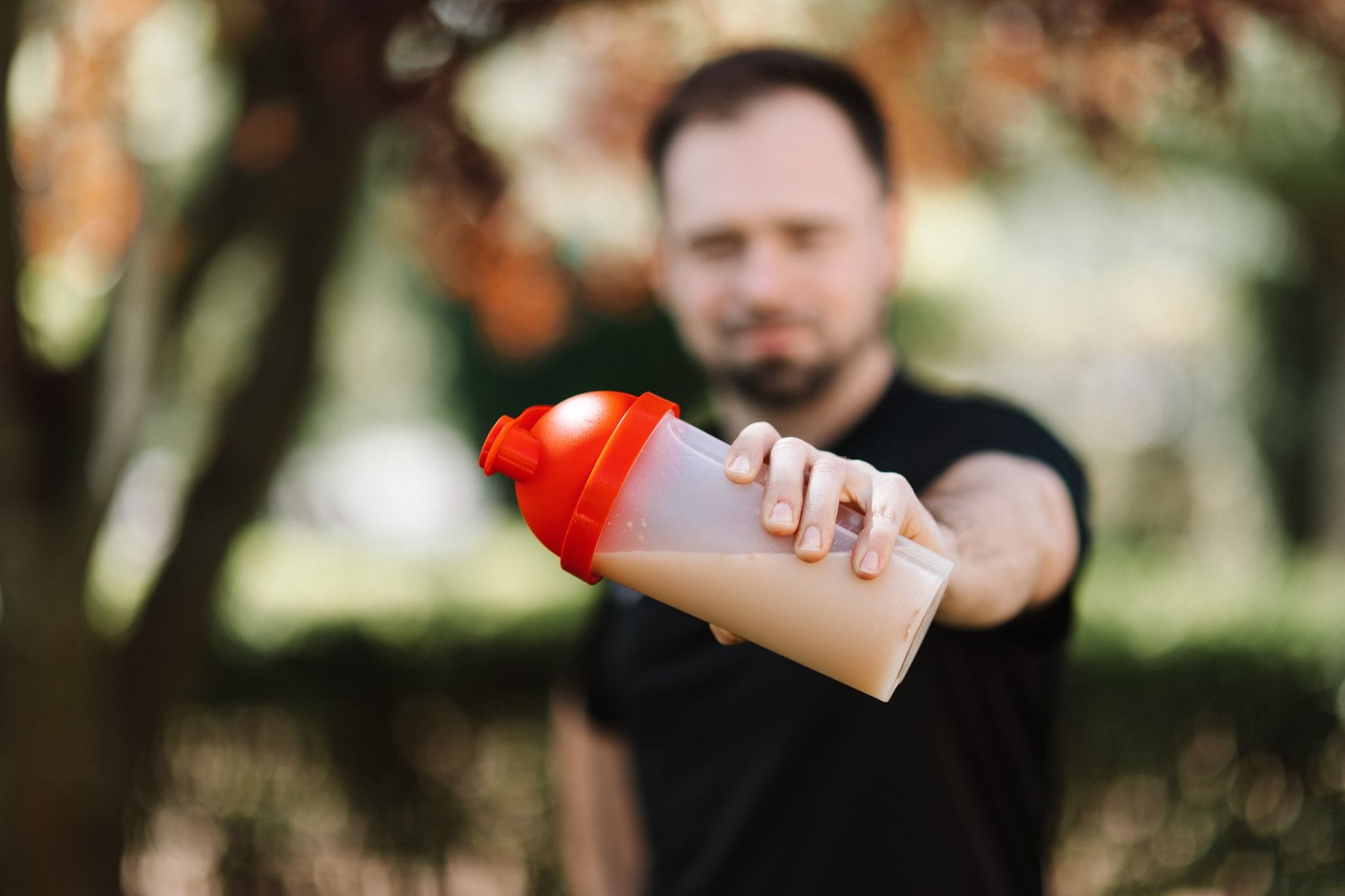 Mężczyzna trzymający shaker z odżywką białkową na tle zieleni