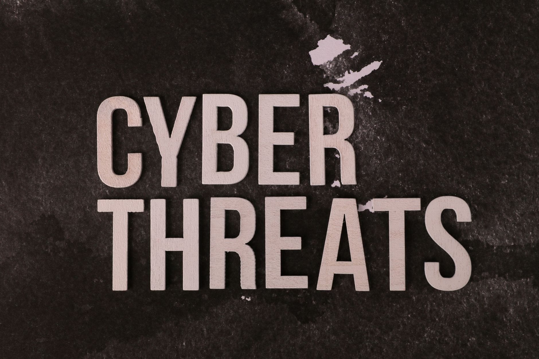 Napis Cyber Threats na ciemnym, fakturowanym tle nawiązujący do cyberprzestępczo